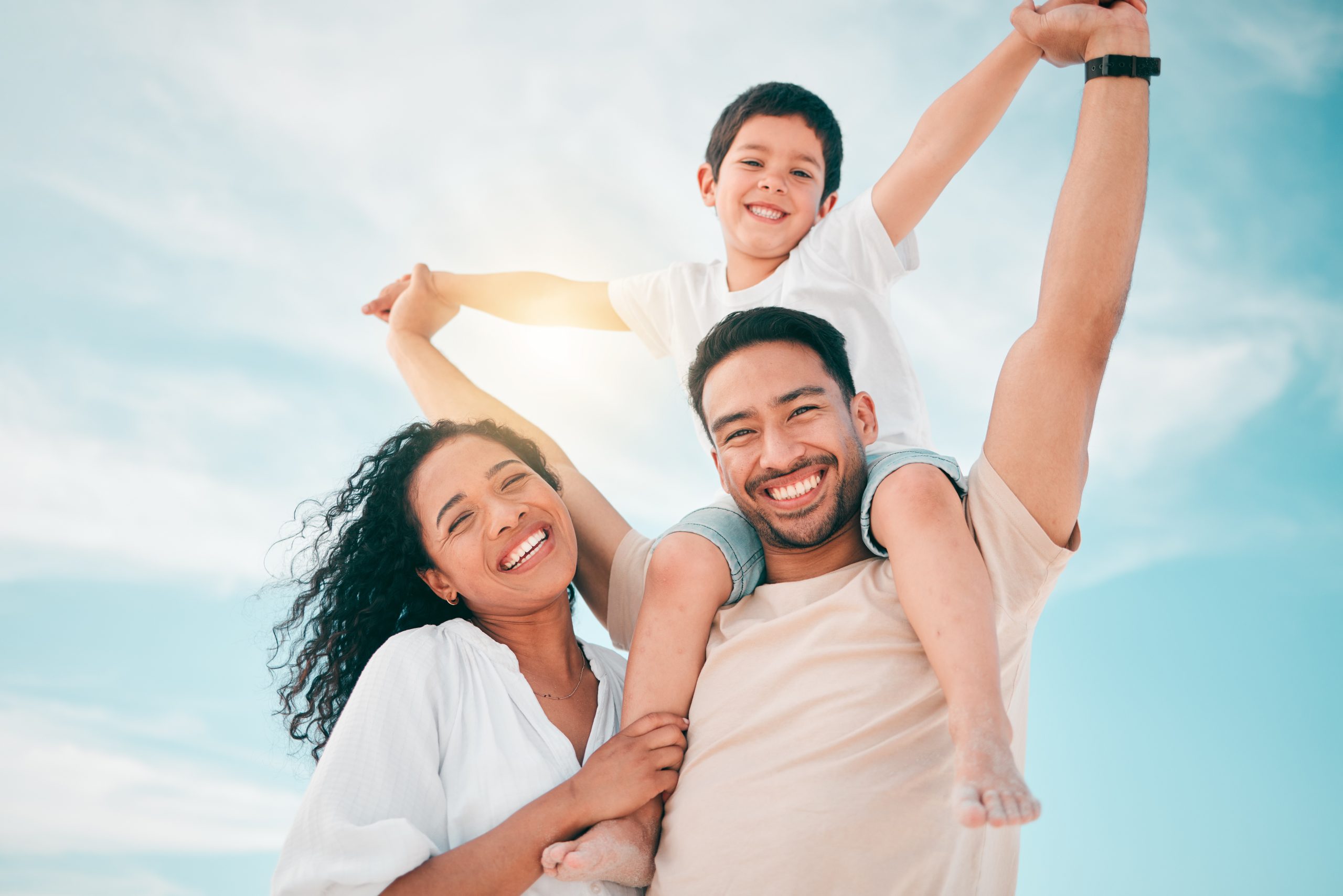 Happy family, portrait and airplane games at a beach with freedom, bond and fun together on blue sky background. Face, love and piggyback by parents and boy child outdoor for travel, holiday or trip